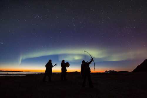 Three people standing under the northern lights